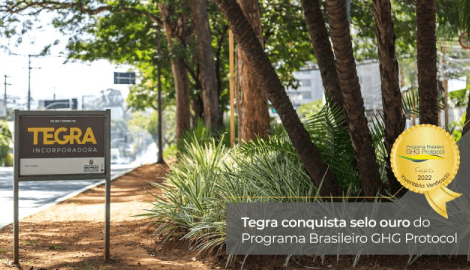 Um ambiente urbano, no canto esquerdo temos uma placa da Tegra Incorporadora e no canto direito temos algumas arvores